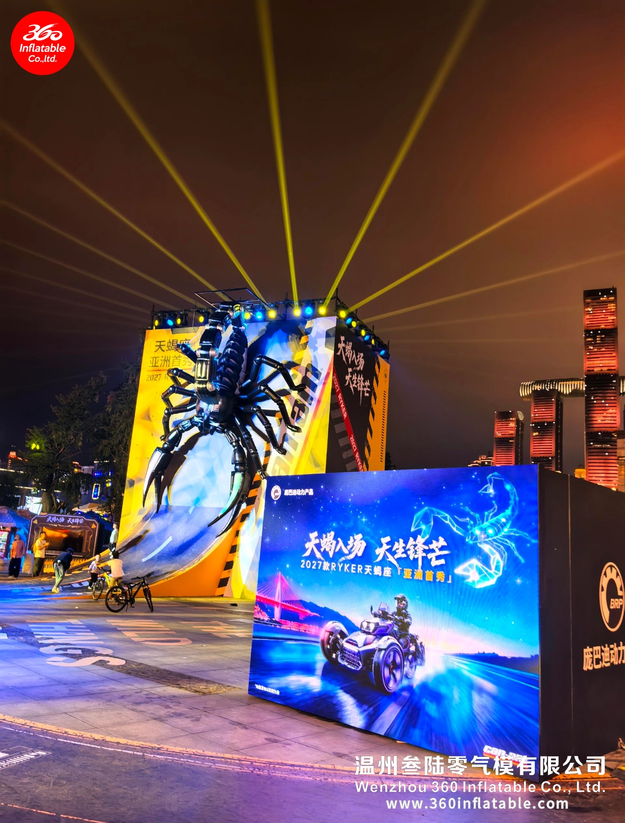 Panoramic view of the outdoor plaza featuring a glowing Can-Am Ryker billboard, riding demo area, and the giant mechanical scorpion inflatable.